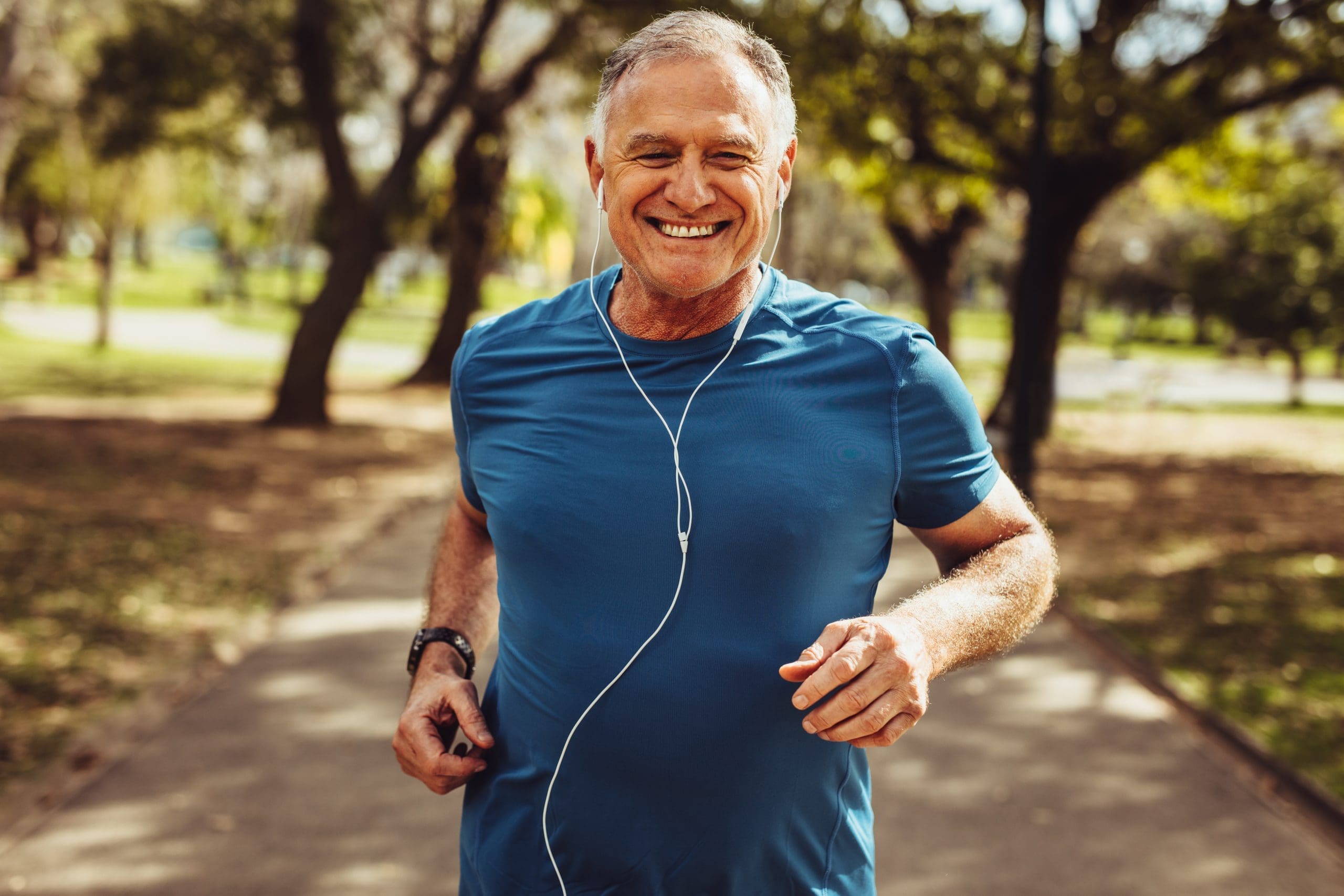 Senior man working out for good health Close up of a smiling man running while listening to music using earphones.