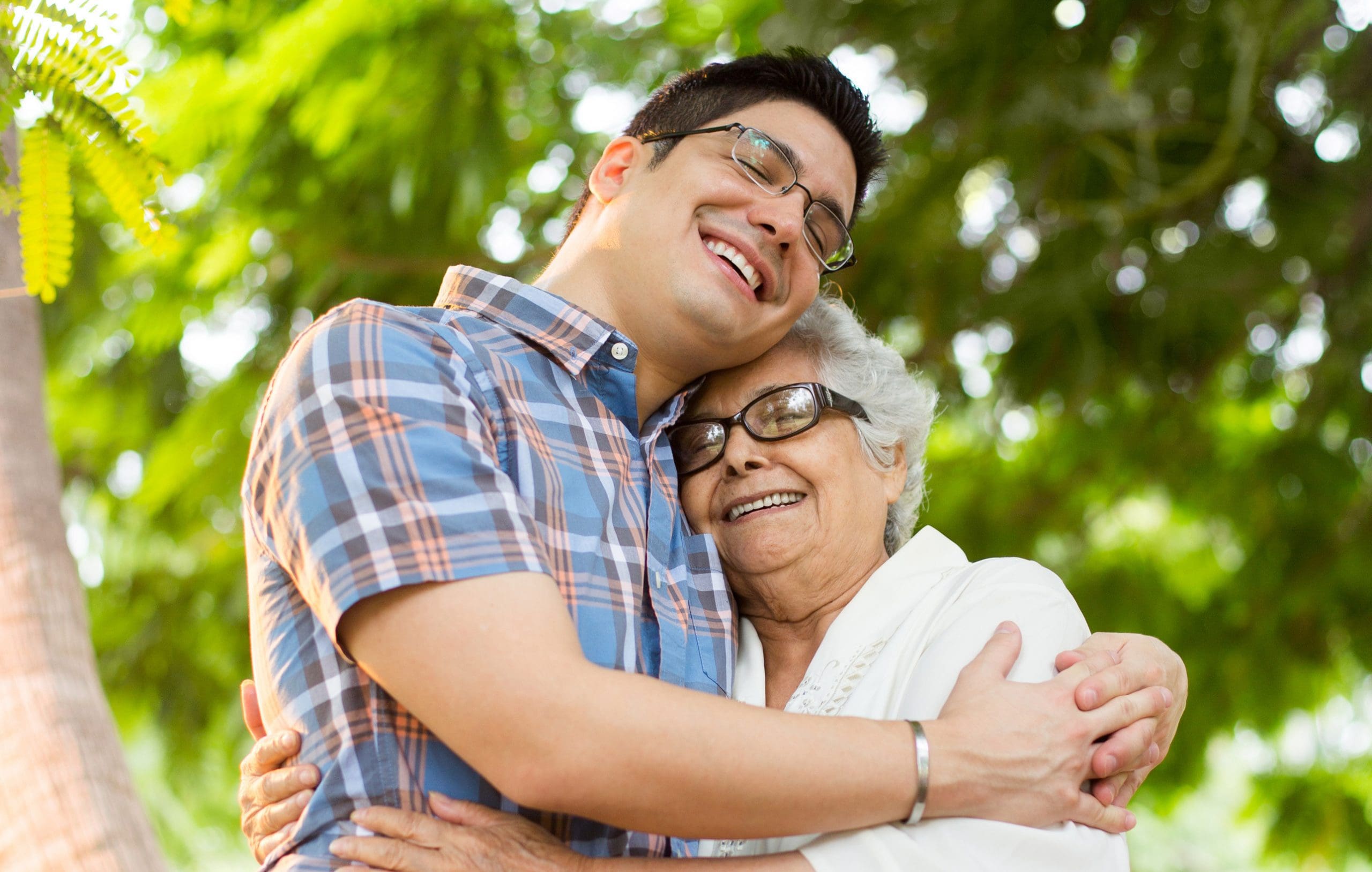 A latin senior woman and her grandson embracing and smiling with eyes closed in a vertical medium shot outdoor