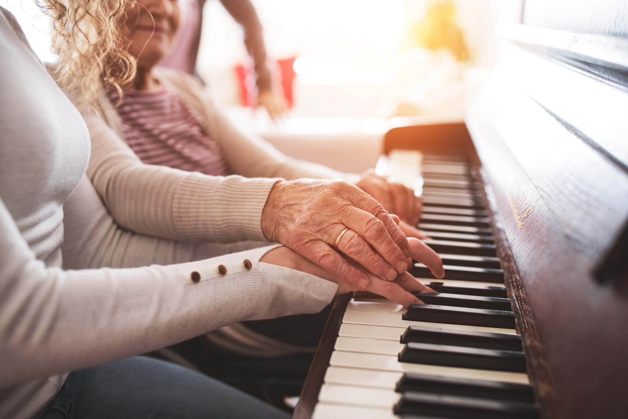 A girl with grandmother playing the piano. An unrecognizable teenage girl with grandmother playing the piano at home. Family and generations concept.