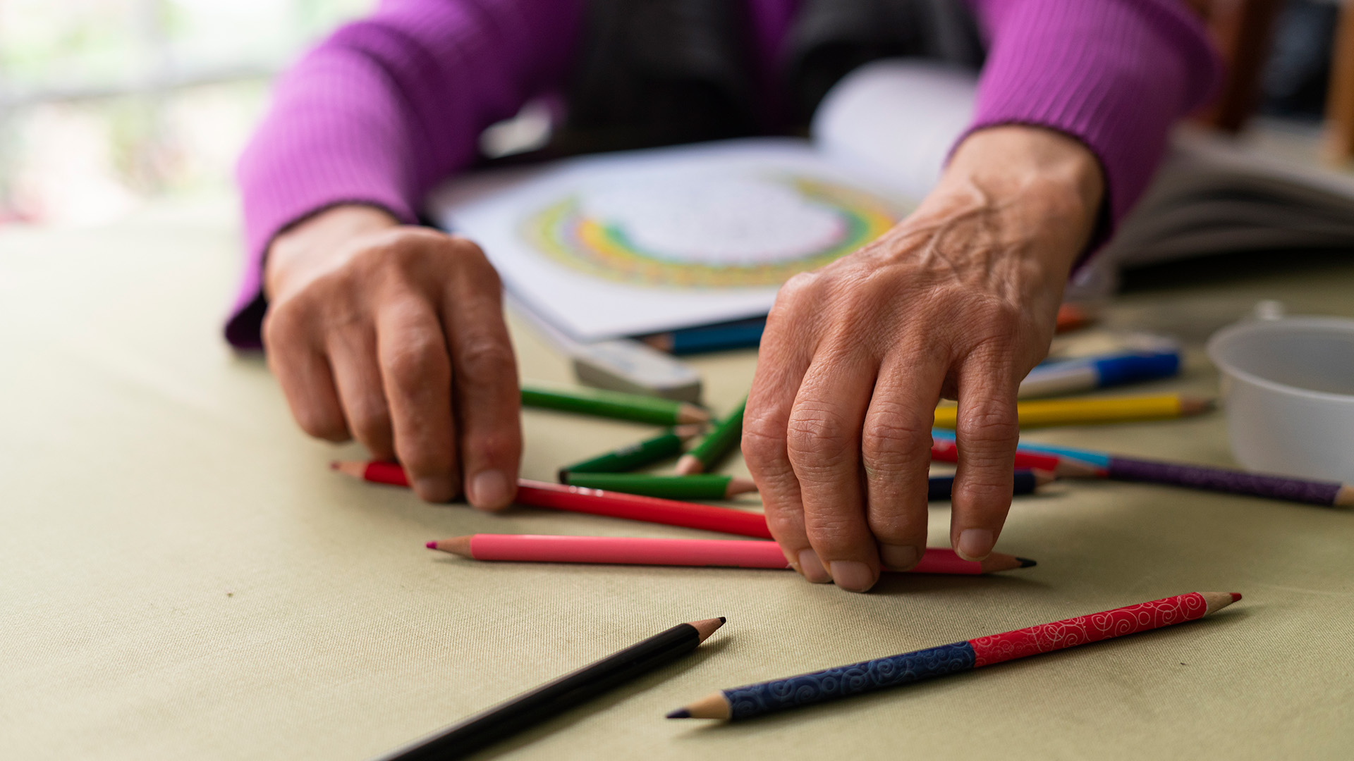 senior hands reaching for colored pencils to draw