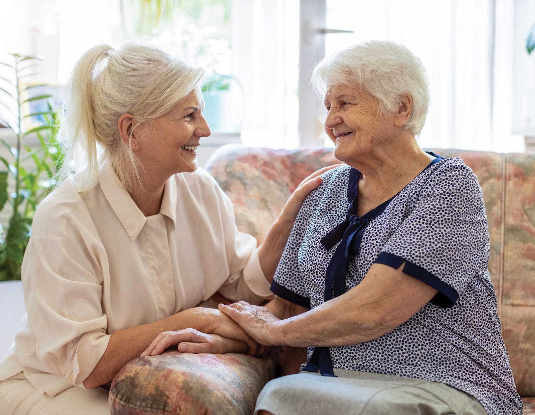 Senior woman sitting on a sofa with her adult daughter - hands clasped
