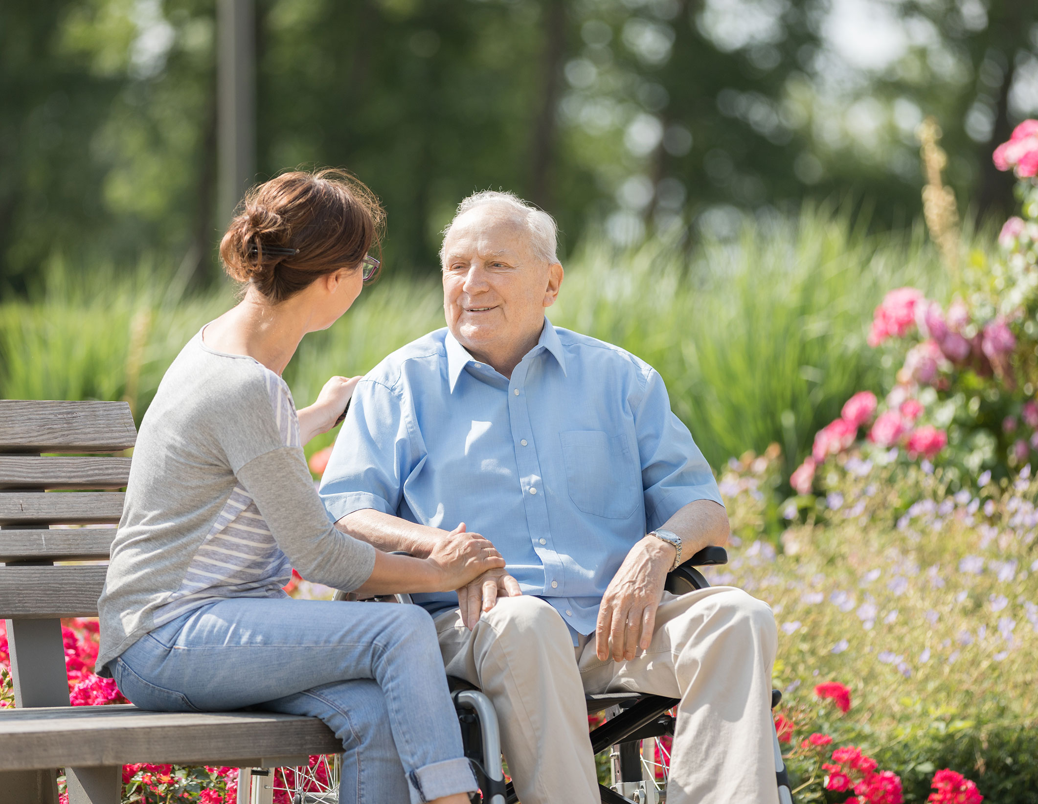 Senior man chatting with his adult daughter outside on a bench