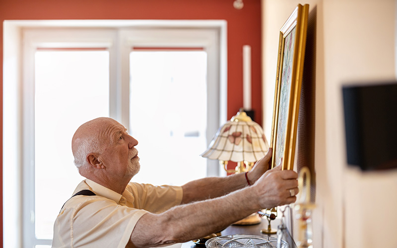 older man hanging art in his senior living apartment
