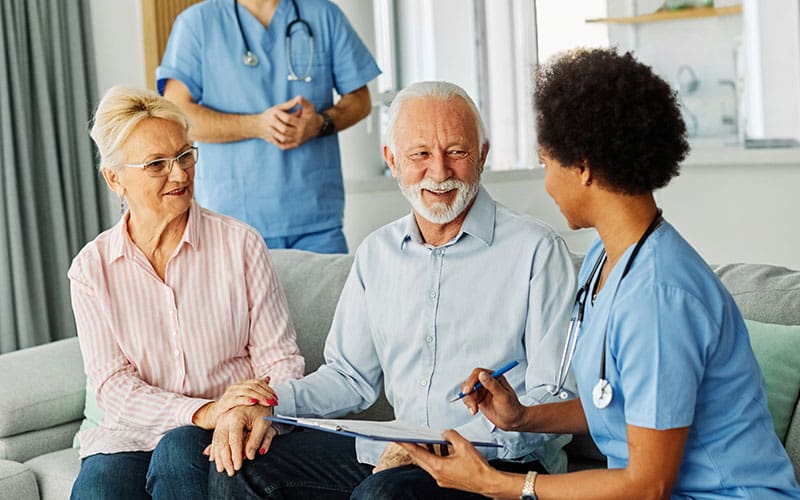 senior couple speaking with a caregiver who is taking notes on a clipboard