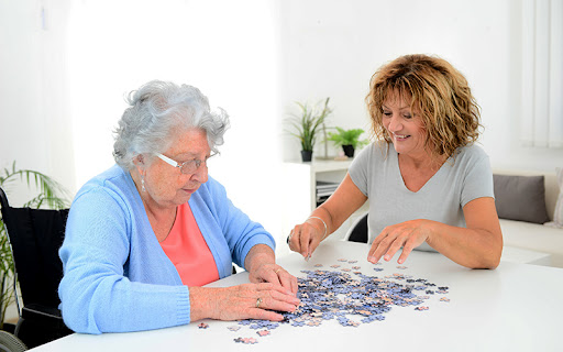 senior woman doing a puzzle with her caregiver in memory care