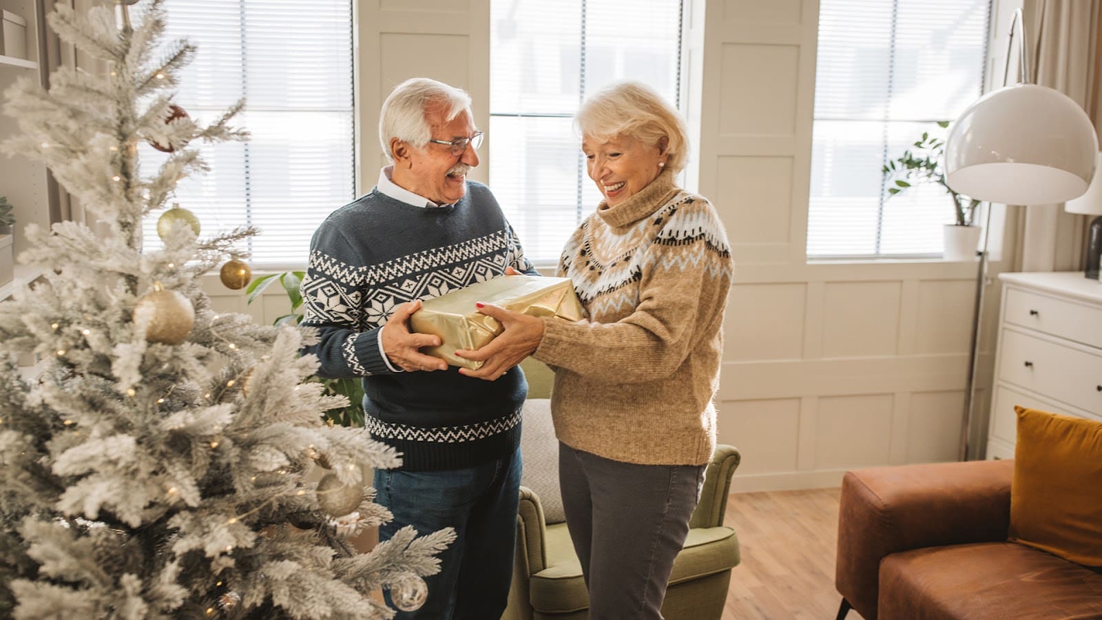 Senior couple opening gifts next to a Christmas tree