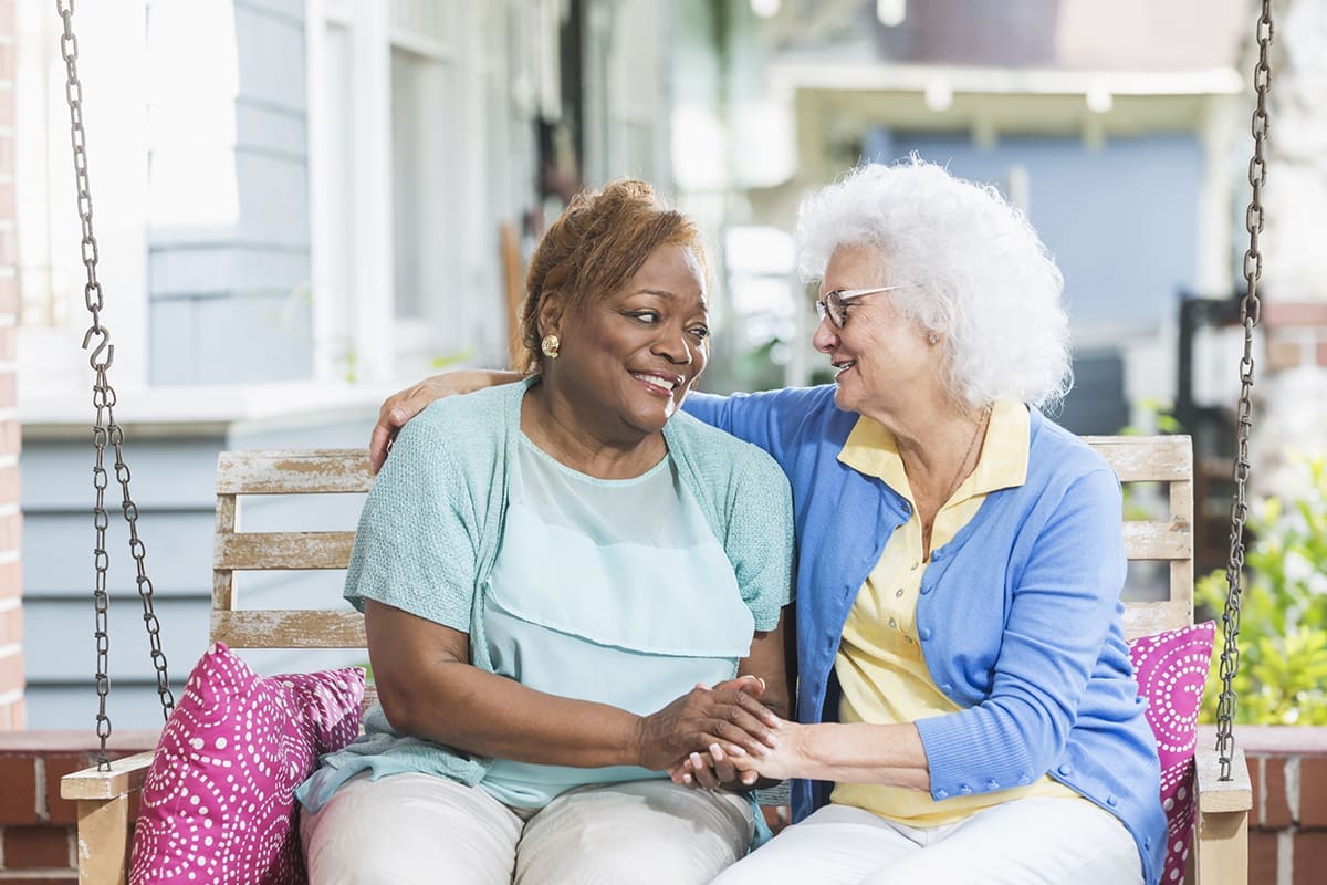 Two senior women sitting on a porch swing, smiling and sharing a moment of friendship at Quartet Senior Living in Bettendorf, IA